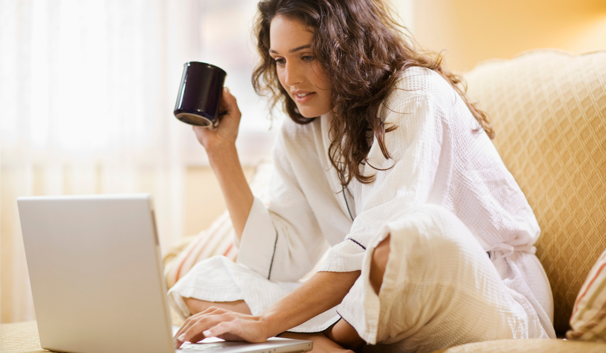 Femme en peignoir installée avec son ordinateur portable et un café