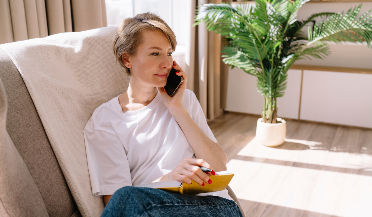 Femme souriante en appel téléphonique installée sur son canapé